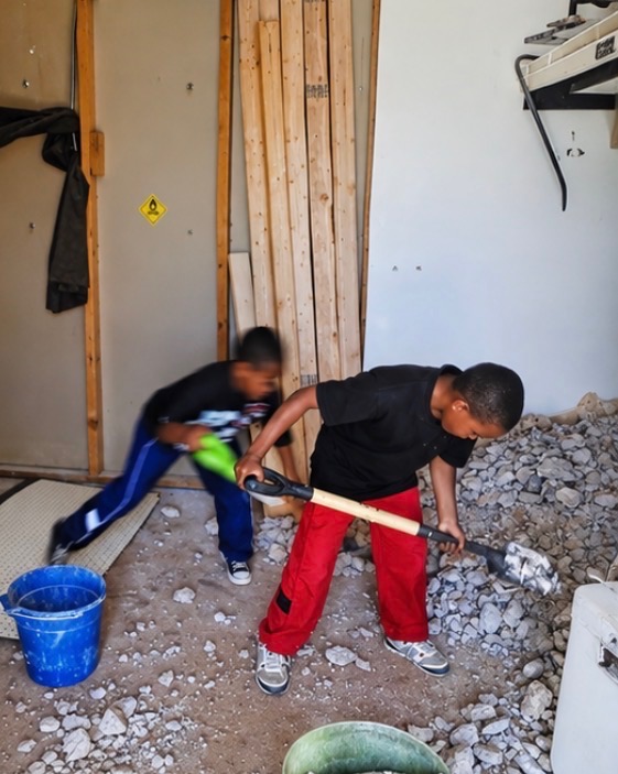 Two boys shoveling broken concrete during a renovation